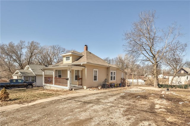 view of side of home with a porch, roof with shingles, and a chimney