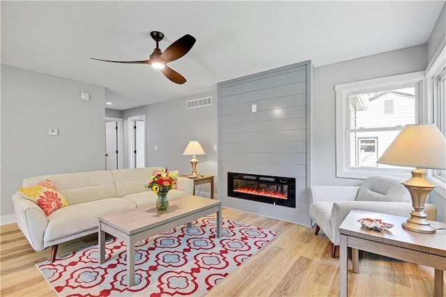 living area featuring visible vents, a large fireplace, ceiling fan, light wood-type flooring, and baseboards