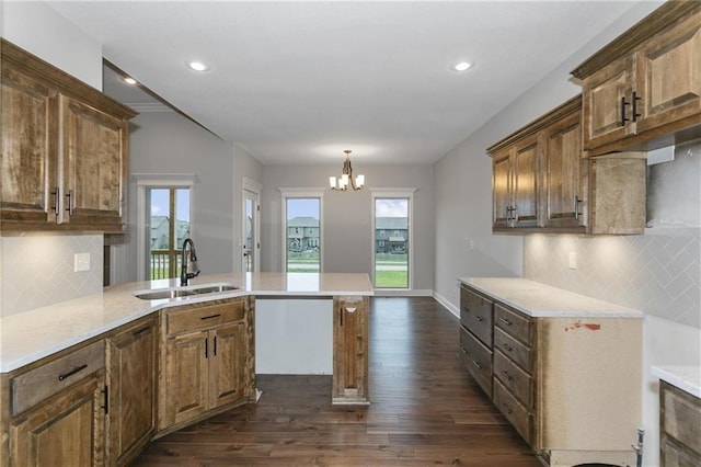 kitchen with dark wood finished floors, hanging light fixtures, an inviting chandelier, brown cabinetry, and a sink