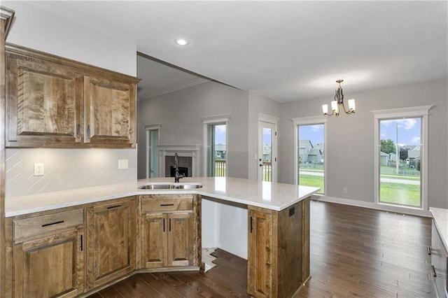 kitchen with dark wood-style floors, hanging light fixtures, brown cabinetry, open floor plan, and a sink