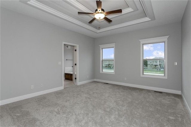 unfurnished room with a tray ceiling, light colored carpet, visible vents, a ceiling fan, and baseboards