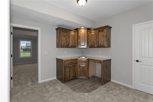 kitchen featuring carpet floors, baseboards, light countertops, and a sink