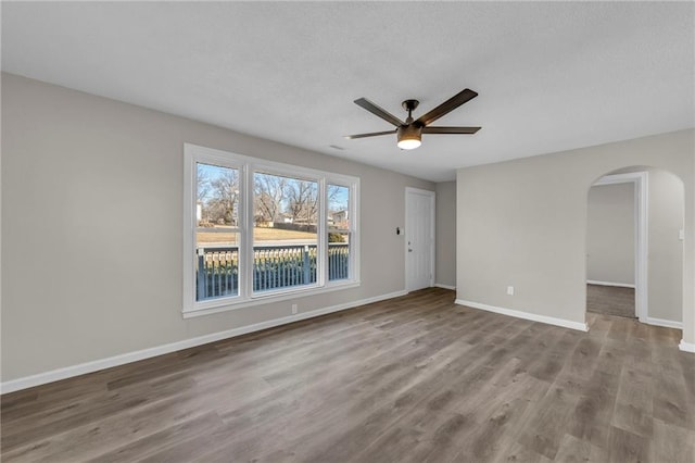 unfurnished room with a ceiling fan, baseboards, arched walkways, and wood finished floors