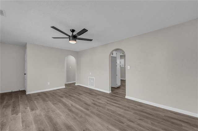 unfurnished room featuring a ceiling fan, arched walkways, visible vents, and wood finished floors