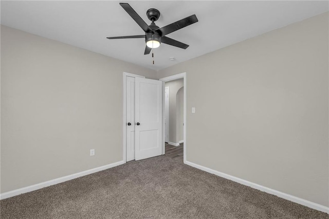 carpeted spare room featuring baseboards, arched walkways, and a ceiling fan