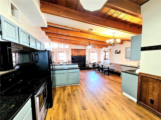 kitchen with light wood-style flooring, stainless steel range with electric cooktop, black microwave, beam ceiling, and ceiling fan with notable chandelier