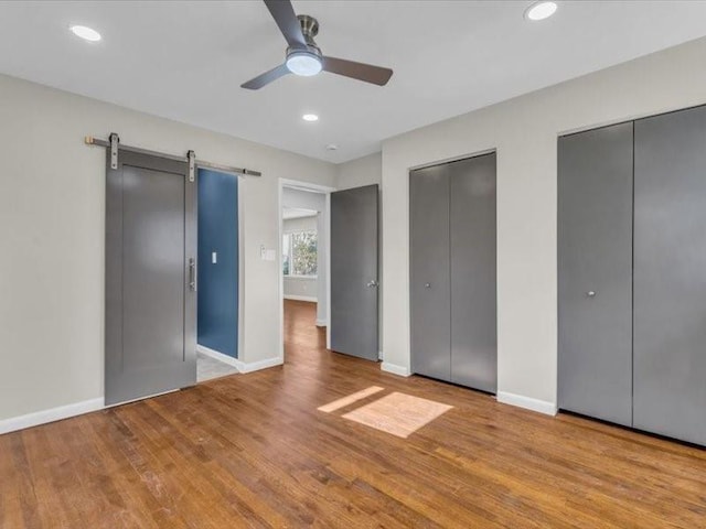 unfurnished bedroom with multiple closets, wood finished floors, baseboards, and a barn door