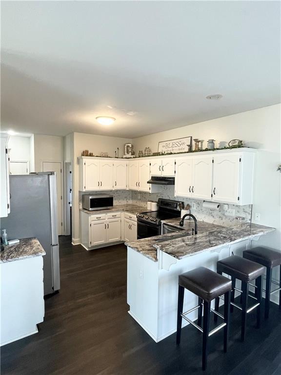 kitchen featuring under cabinet range hood, stainless steel appliances, a peninsula, a kitchen breakfast bar, and white cabinets