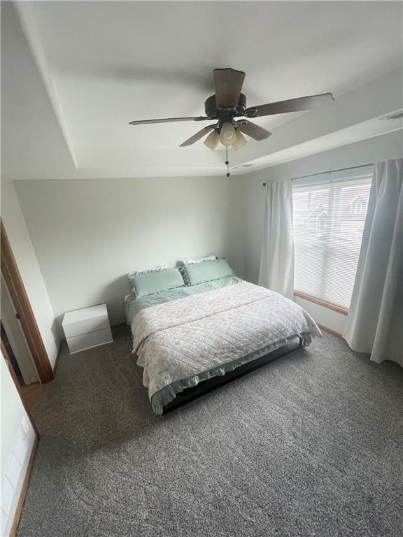 carpeted bedroom featuring a tray ceiling, a ceiling fan, and baseboards