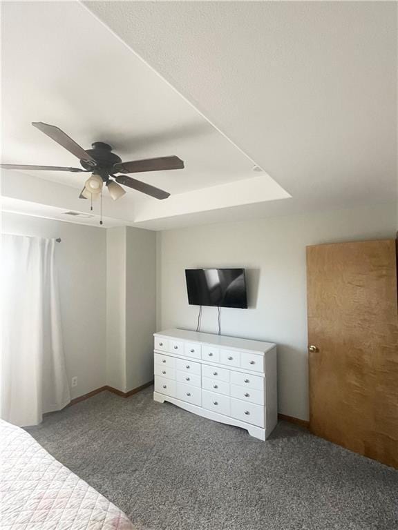 unfurnished bedroom with a ceiling fan, dark colored carpet, and a raised ceiling