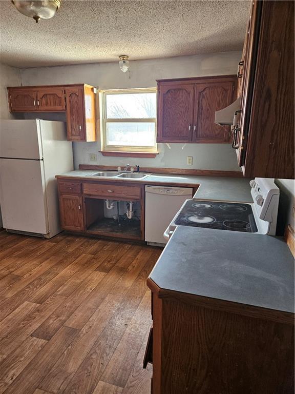 kitchen with light countertops, white appliances, brown cabinetry, and a sink