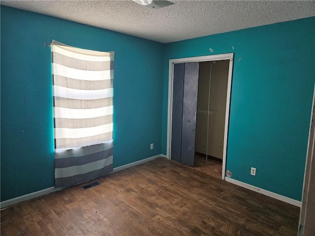 unfurnished bedroom with a textured ceiling, dark wood finished floors, and baseboards