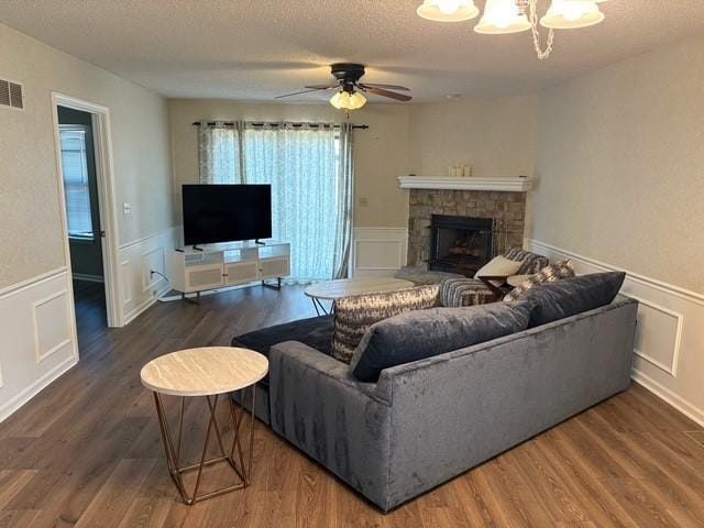 living area with a wainscoted wall, dark wood-style flooring, a textured ceiling, a stone fireplace, and a decorative wall