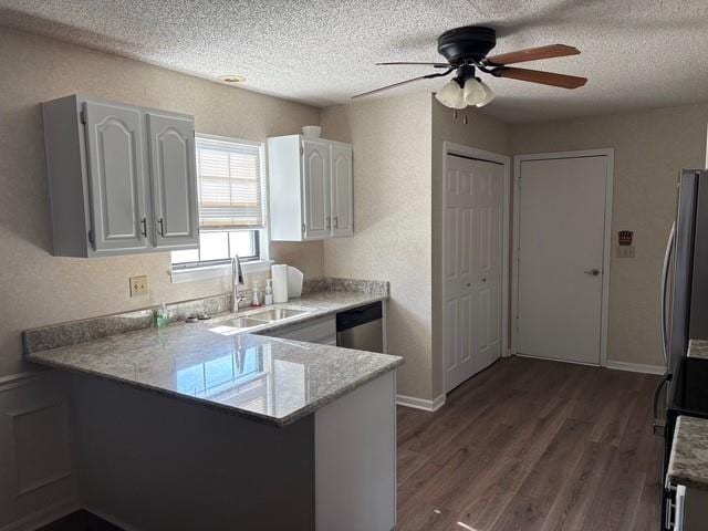 kitchen with white cabinets, dark wood-style floors, a peninsula, stainless steel appliances, and a sink