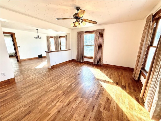 empty room featuring wood-type flooring, baseboards, and ceiling fan with notable chandelier