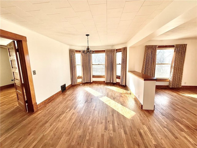 unfurnished dining area with a chandelier, wood finished floors, a wealth of natural light, and baseboards