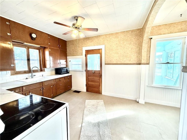 kitchen featuring electric stove, a wainscoted wall, light countertops, a sink, and black microwave