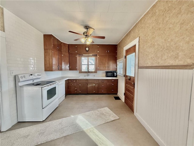 kitchen featuring a wainscoted wall, light tile patterned floors, light countertops, a sink, and white appliances