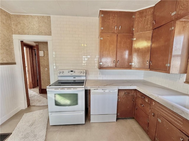 kitchen with light tile patterned floors, light countertops, backsplash, brown cabinetry, and white appliances