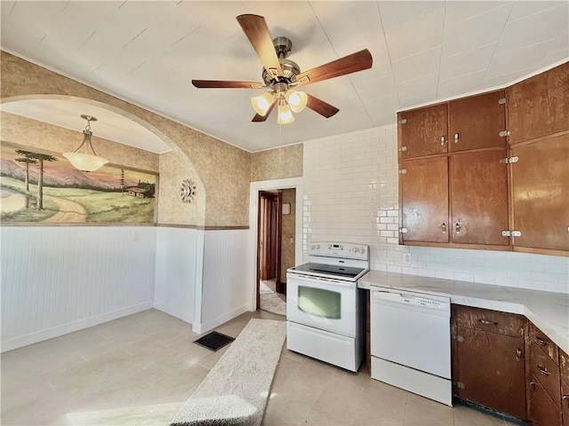 kitchen with light countertops, backsplash, a ceiling fan, wainscoting, and white appliances