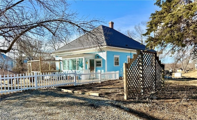 view of side of property with metal roof, a fenced front yard, and a chimney