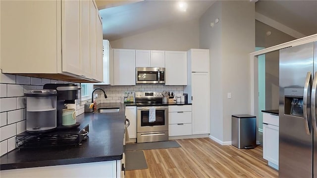 kitchen featuring vaulted ceiling, dark countertops, a sink, light wood-type flooring, and stainless steel appliances