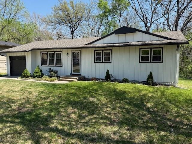 ranch-style house with board and batten siding, an attached garage, a shingled roof, and a front lawn