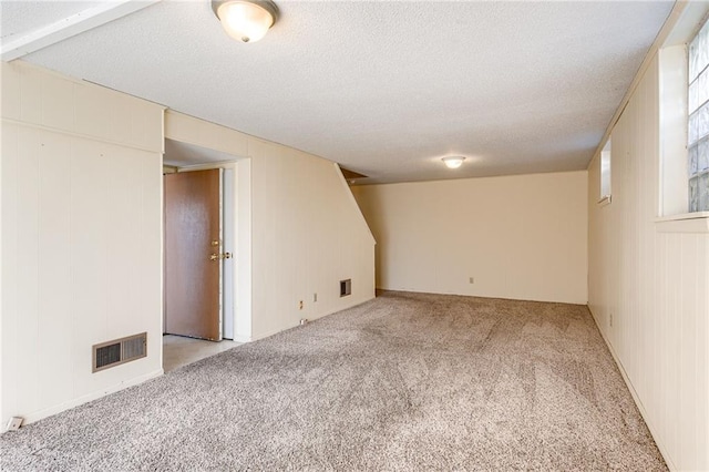 finished below grade area featuring light colored carpet, visible vents, and a textured ceiling