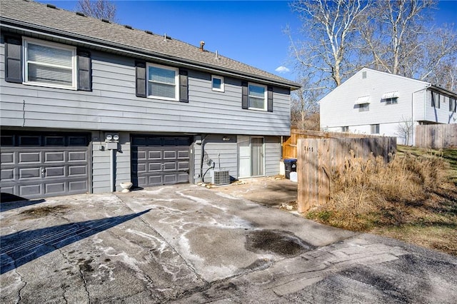 view of property exterior with central air condition unit, a shingled roof, concrete driveway, fence, and a garage