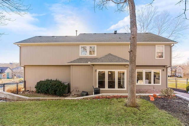 rear view of house with roof with shingles, fence, and a yard