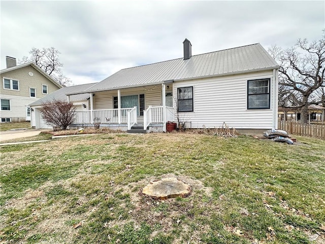 view of front of home with metal roof, covered porch, a garage, a front lawn, and a chimney