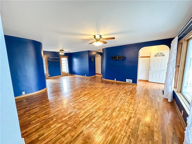 unfurnished living room featuring visible vents, arched walkways, ceiling fan, wood finished floors, and a wealth of natural light