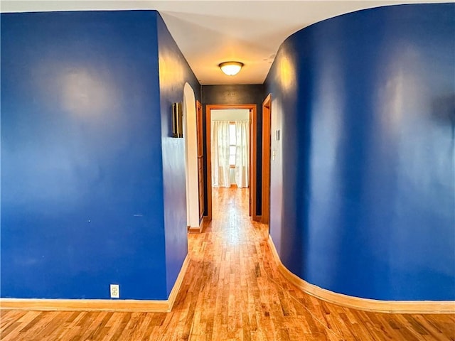 hall featuring arched walkways, wood finished floors, and baseboards