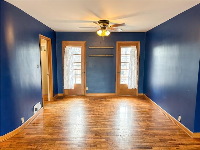 spare room with a ceiling fan, visible vents, baseboards, and wood finished floors