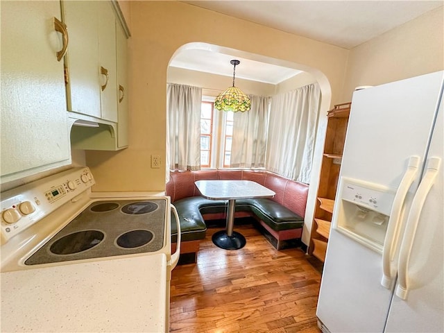 kitchen with white appliances, light wood finished floors, arched walkways, breakfast area, and decorative light fixtures