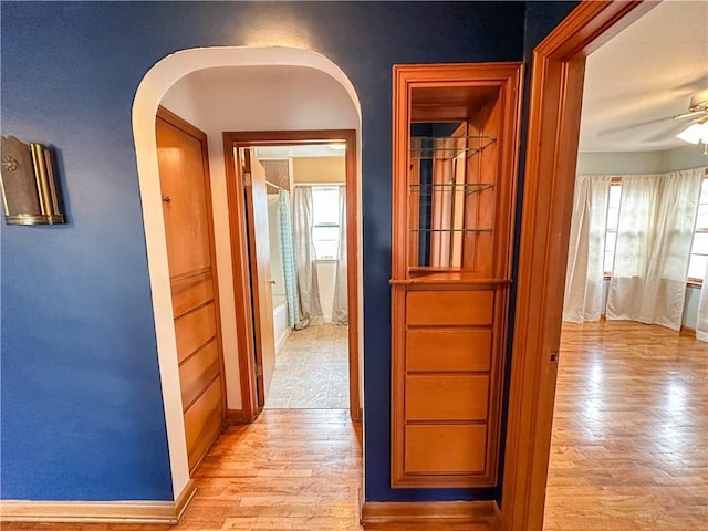 corridor with light wood-style floors, baseboards, and arched walkways