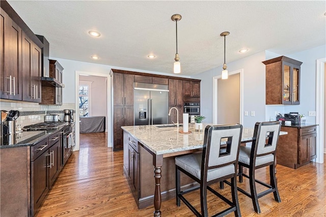 kitchen with stainless steel appliances, light wood-type flooring, wall chimney range hood, a kitchen bar, and a sink