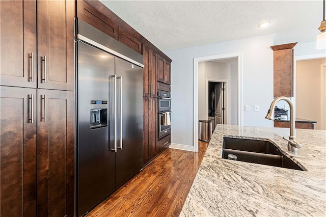 kitchen featuring a textured ceiling, dark wood-style flooring, a sink, light stone countertops, and stainless steel built in refrigerator