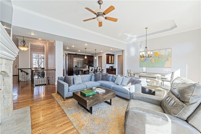 living room featuring light wood-type flooring, a tray ceiling, crown molding, and ceiling fan with notable chandelier