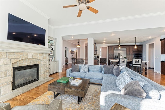 living room featuring ceiling fan, a stone fireplace, wood finished floors, baseboards, and ornamental molding