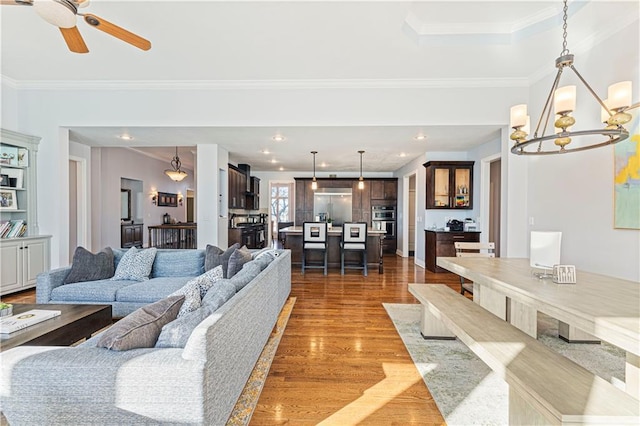 living room with ceiling fan with notable chandelier, recessed lighting, crown molding, and wood finished floors