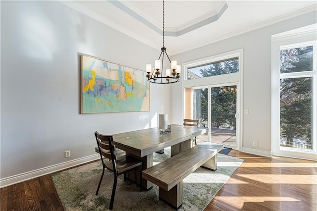 dining space with baseboards, ornamental molding, wood finished floors, an inviting chandelier, and a tray ceiling