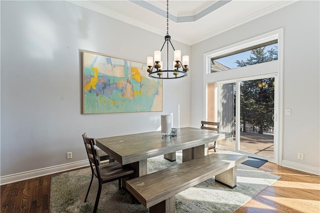 dining space featuring a chandelier, wood finished floors, baseboards, ornamental molding, and a tray ceiling