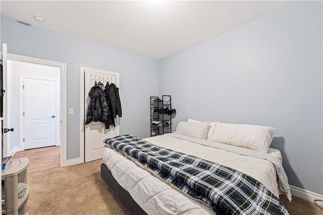 bedroom with light carpet, a textured ceiling, and baseboards