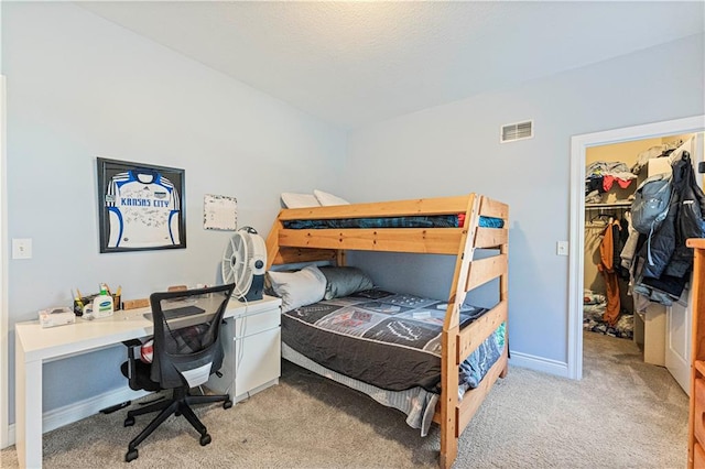 carpeted bedroom featuring a spacious closet, visible vents, and baseboards