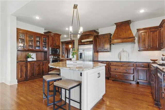 kitchen featuring a kitchen island, backsplash, dark wood finished floors, custom exhaust hood, and stainless steel appliances