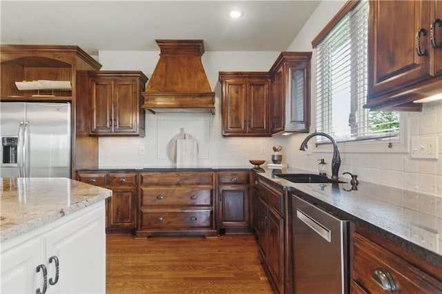 kitchen featuring decorative backsplash, light stone countertops, custom range hood, a sink, and stainless steel appliances