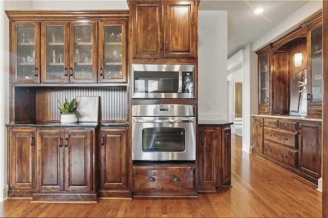 kitchen featuring dark countertops, appliances with stainless steel finishes, recessed lighting, wood finished floors, and glass insert cabinets