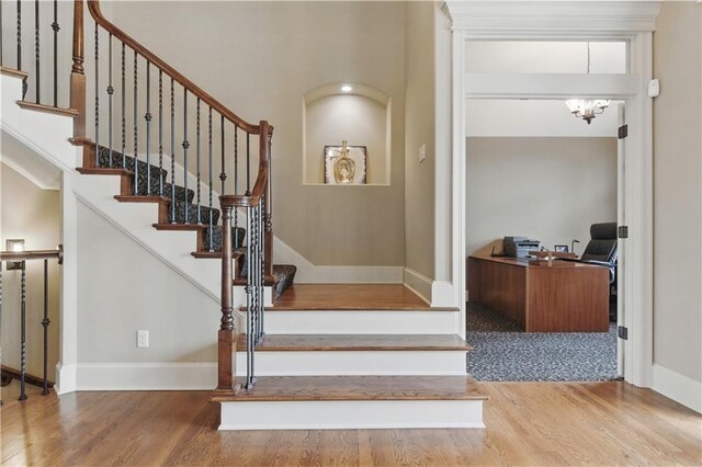 staircase with baseboards, wood finished floors, and a notable chandelier