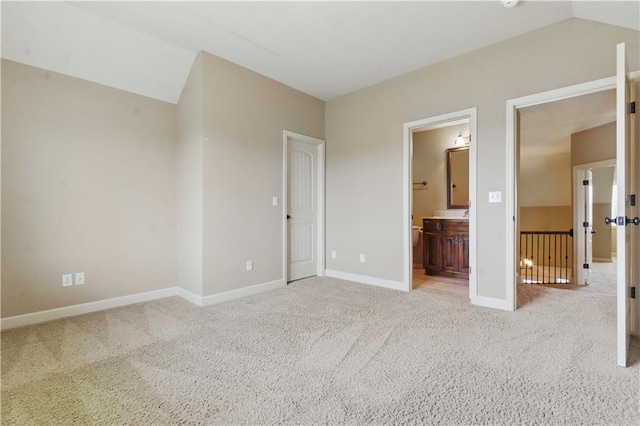 unfurnished bedroom featuring connected bathroom, baseboards, vaulted ceiling, and light carpet